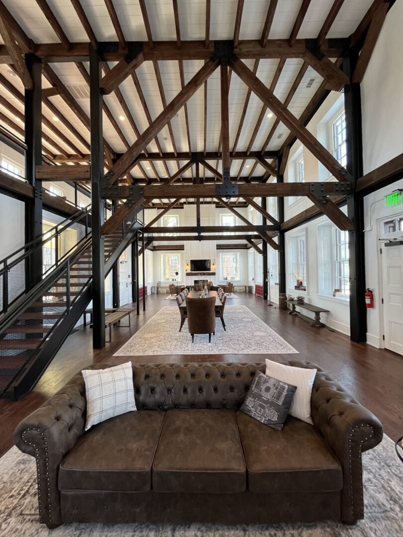 Interior of a barndominium in Longview with white walls, dark timber beams, and a brown leather couch