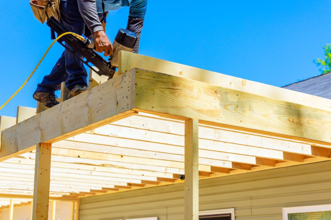 A worker using a nail gun building an elevated deck on a sunny day.